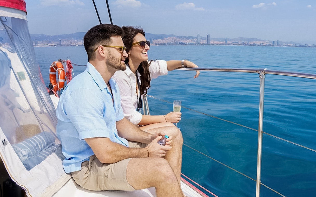 Couple enjoying champagne on a Barcelona cruise with city skyline in the background.