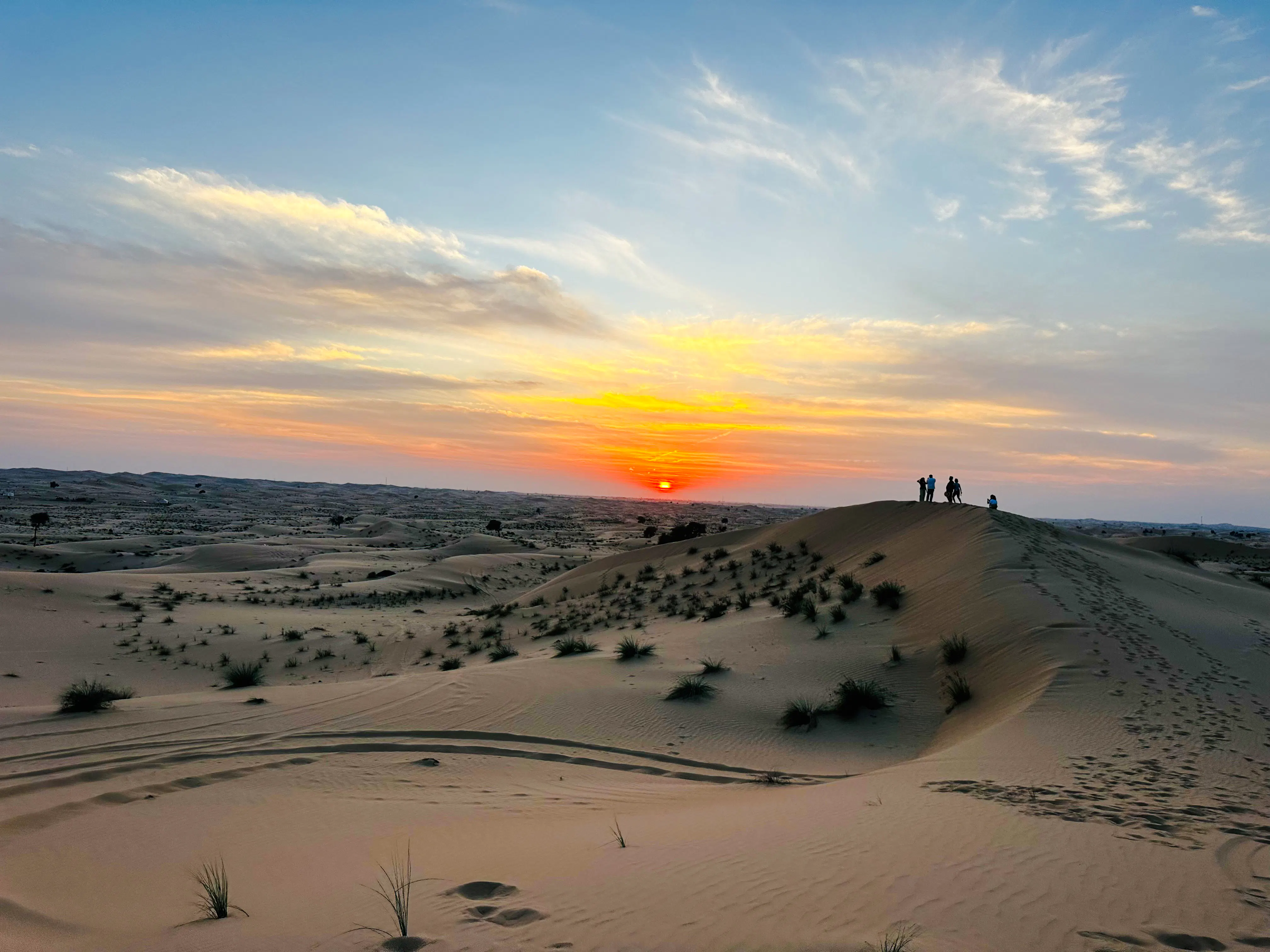 Sunrise over sand dunes with silhouettes of people on a camel ride in Abu Dhabi desert.