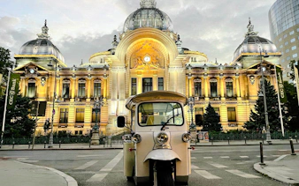 Tuk Tuk in front of illuminated CEC Palace, Bucharest, during highlights tour.