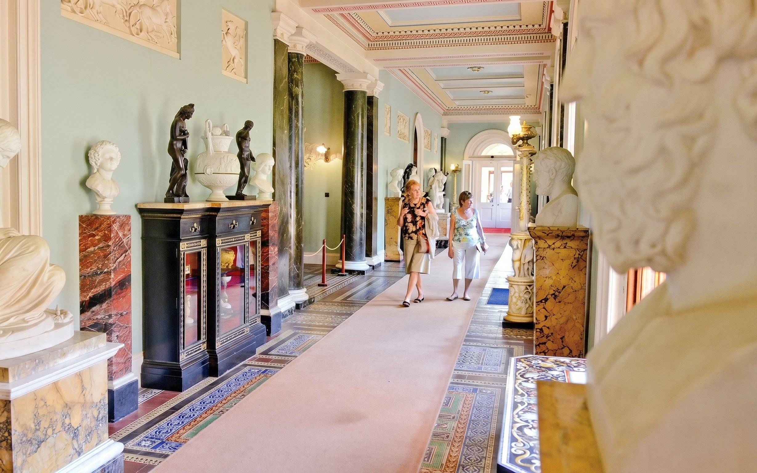 Osborne House interior with sculptures and visitors walking through ornate hallway.