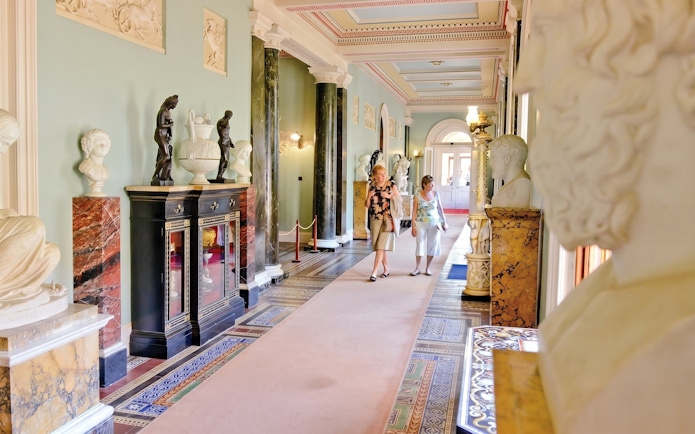 Osborne House interior with sculptures and visitors walking through ornate hallway.