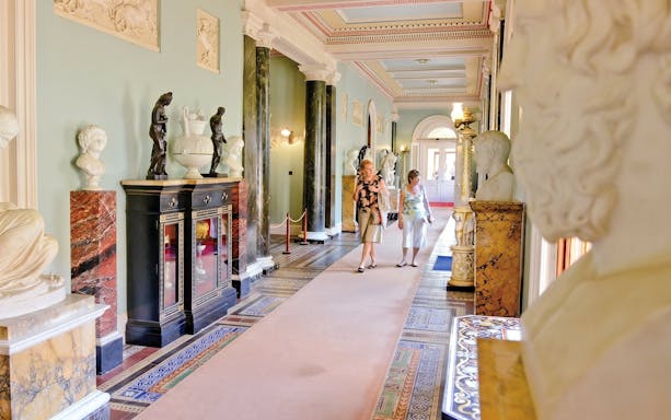 Osborne House interior with sculptures and visitors walking through ornate hallway.