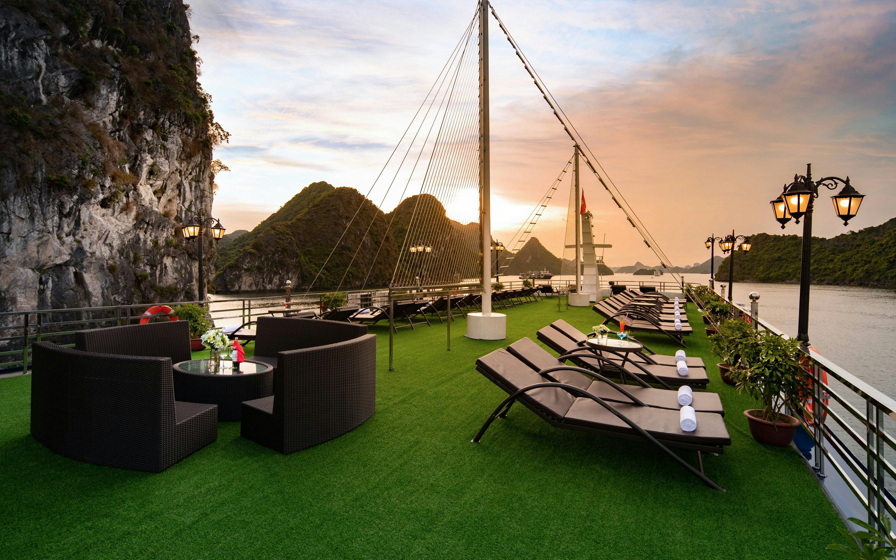Cruise deck with lounge chairs and tables overlooking Lan Ha Bay at sunset.