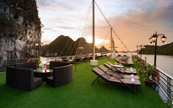 Cruise deck with lounge chairs and tables overlooking Lan Ha Bay at sunset.
