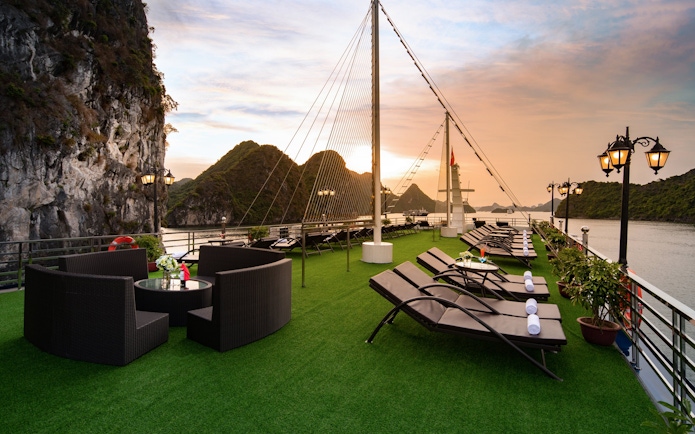Cruise deck with lounge chairs and tables overlooking Lan Ha Bay at sunset.