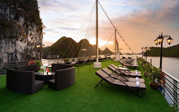 Cruise deck with lounge chairs and tables overlooking Lan Ha Bay at sunset.