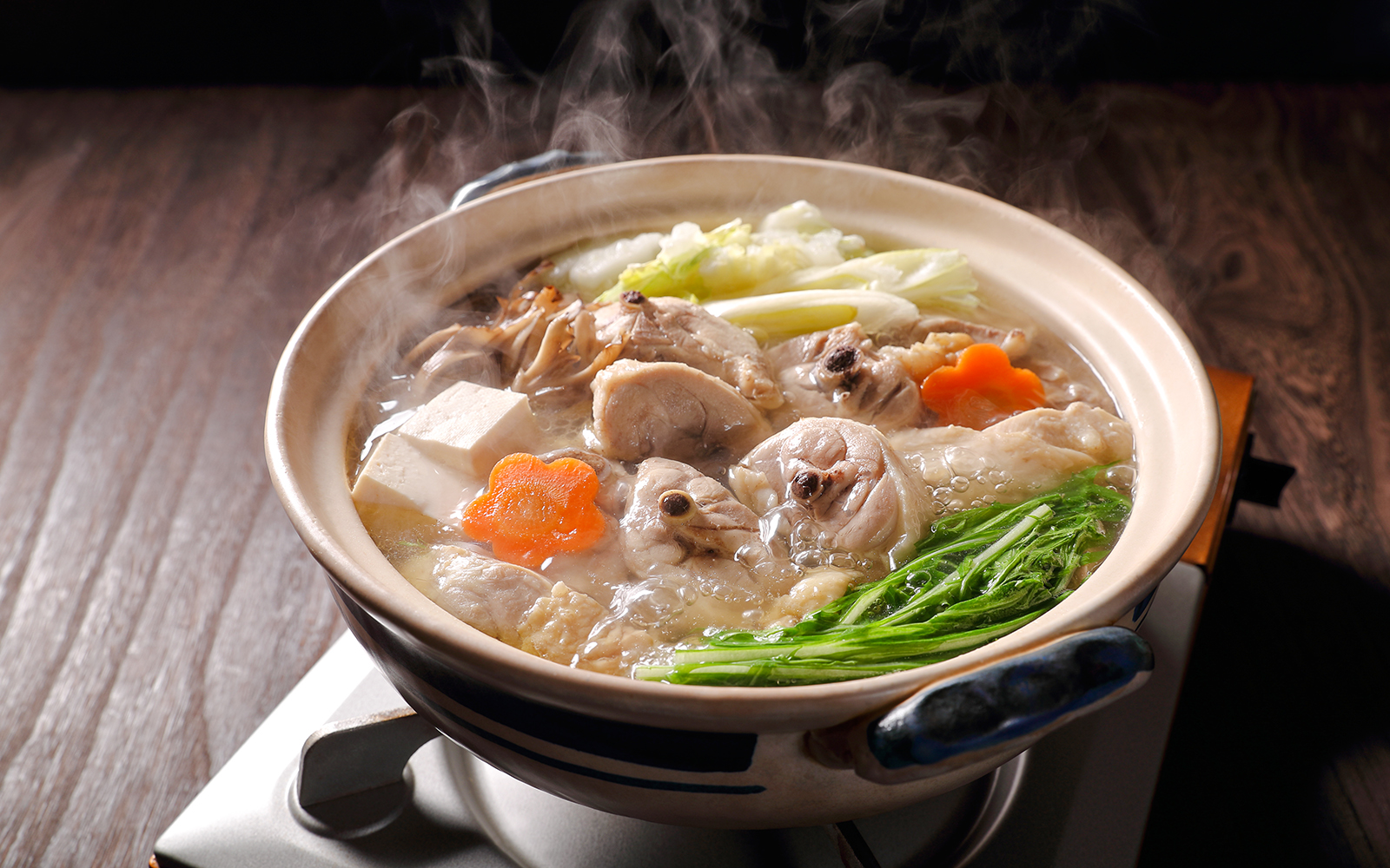 Traditional mizutaki hot pot with vegetables and chicken in a Japanese restaurant setting.