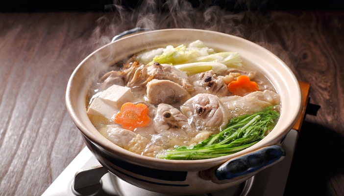Traditional mizutaki hot pot with vegetables and chicken in a Japanese restaurant setting.