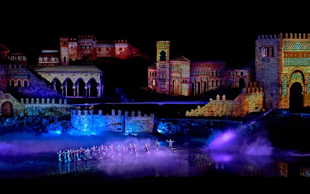 Dancers perform in front of illuminated medieval buildings at Puy du Fou España night show.
