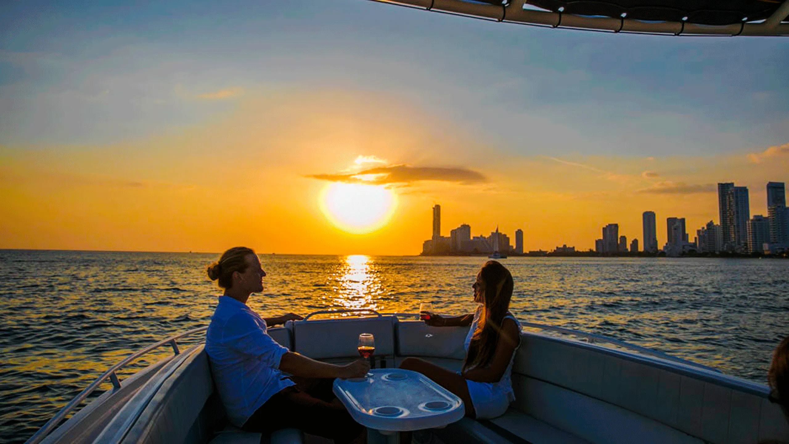 Boat party at sunset in Cartagena Bay with city skyline in the background.