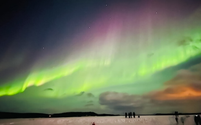Northern lights illuminating the night sky over snowy Lapland landscape.