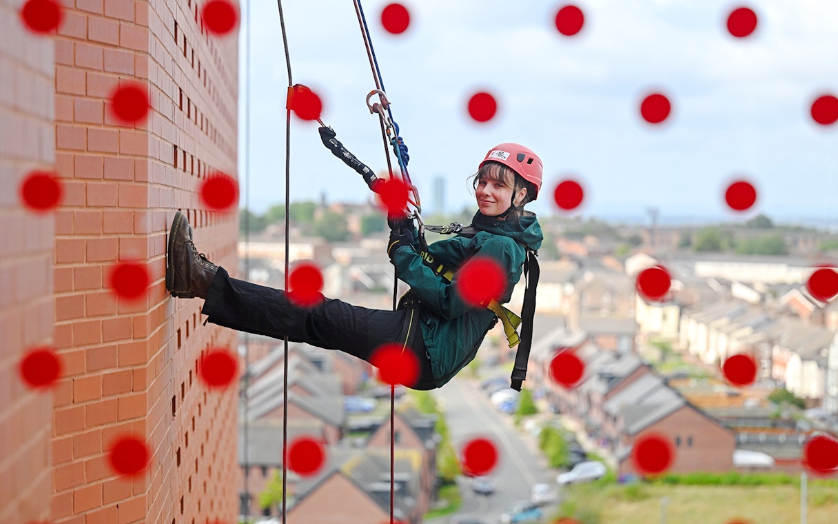 Guest abseiling down Anfield stadium wall with city view in background.