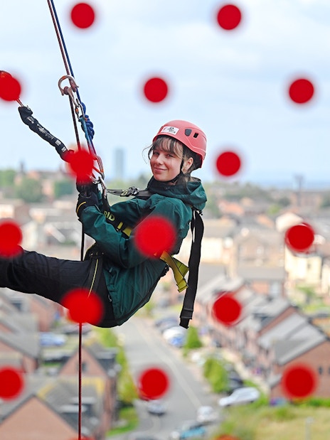 Guest abseiling down Anfield stadium wall with city view in background.