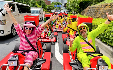 People in colorful costumes driving go-karts on a street in Tokyo Bay.