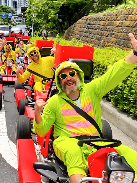 People in colorful costumes driving go-karts on a street in Tokyo Bay.