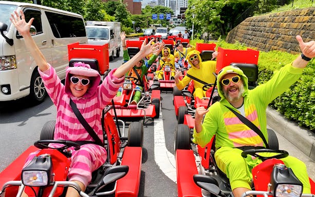People in colorful costumes driving go-karts on a street in Tokyo Bay.