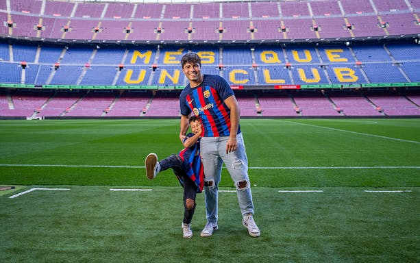 Father and child in FC Barcelona jerseys on Camp Nou field, Barcelona.