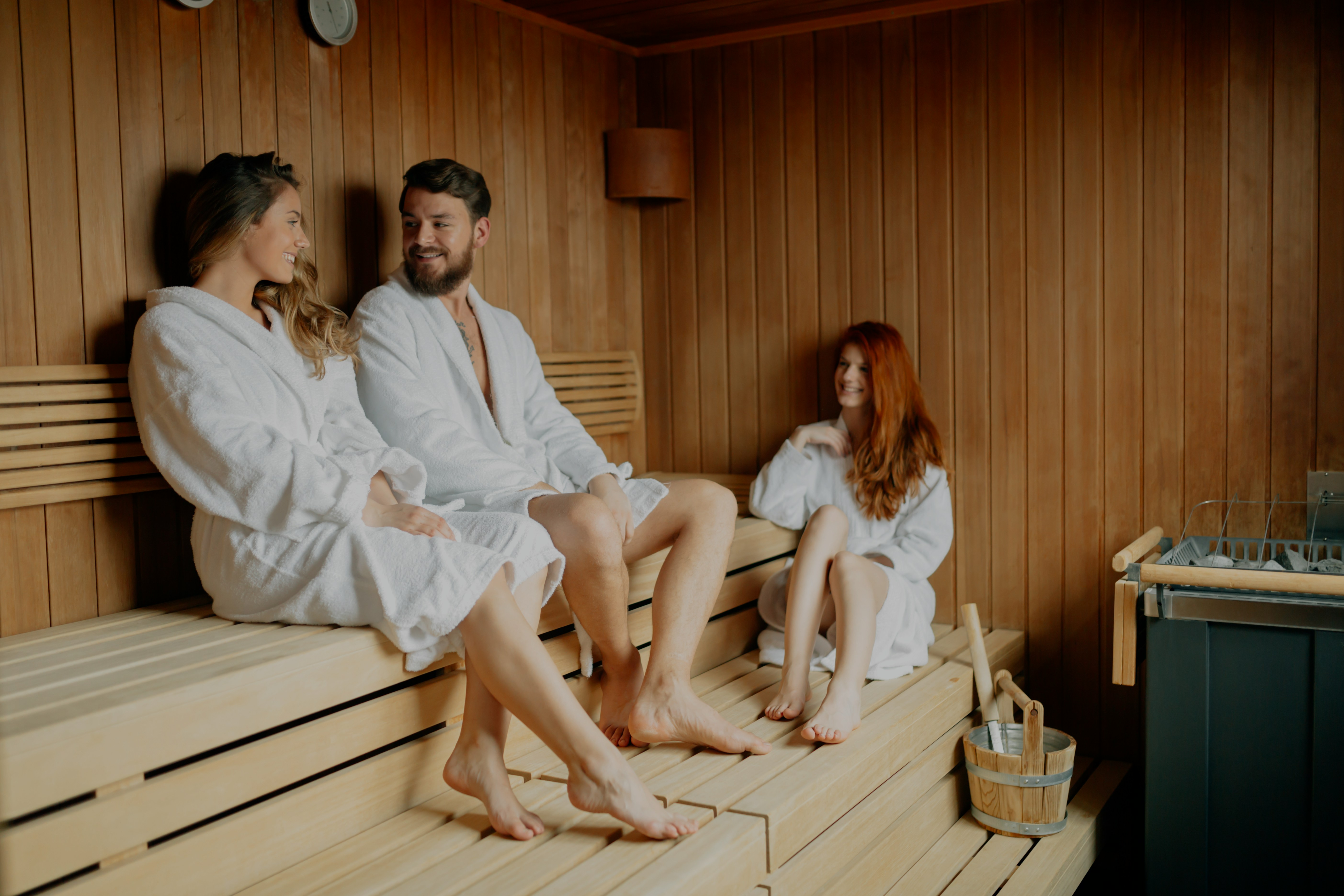 People in white robes relaxing in a wooden sauna.