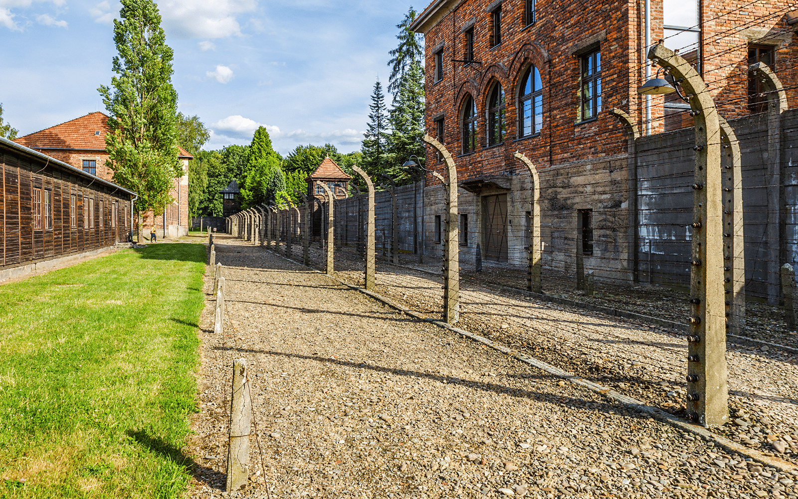Auschwitz I barracks and barbed wire fence under a clear sky.