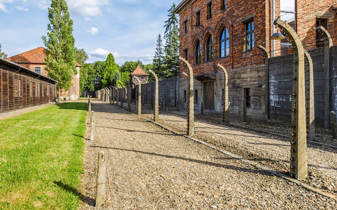Auschwitz I barracks and barbed wire fence under a clear sky.