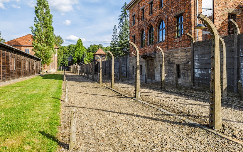 Auschwitz I barracks and barbed wire fence under a clear sky.