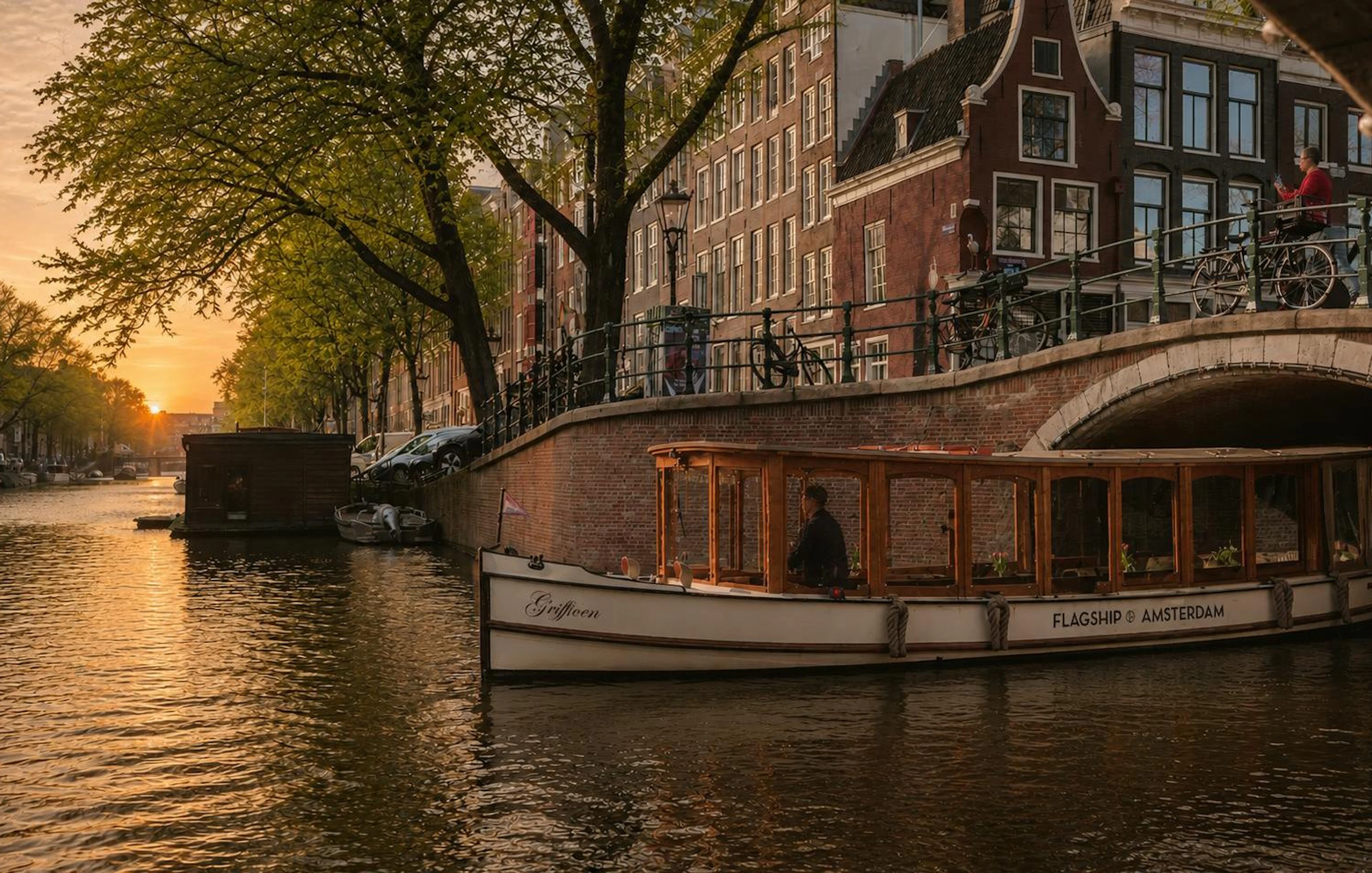 Luxury canal boat cruising under a bridge at sunset in Amsterdam.
