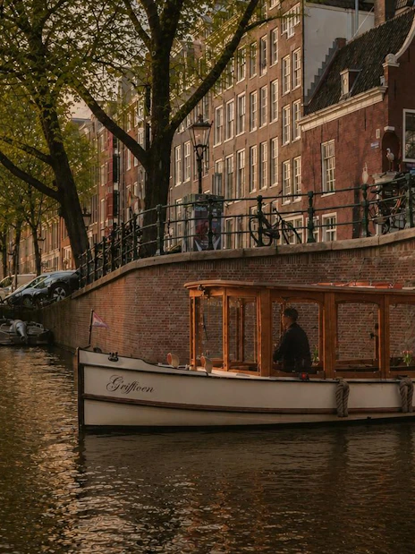 Luxury canal boat cruising under a bridge at sunset in Amsterdam.