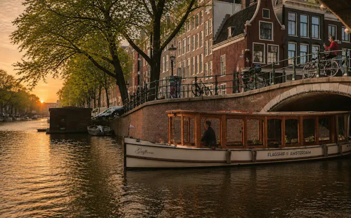 Luxury canal boat cruising under a bridge at sunset in Amsterdam.