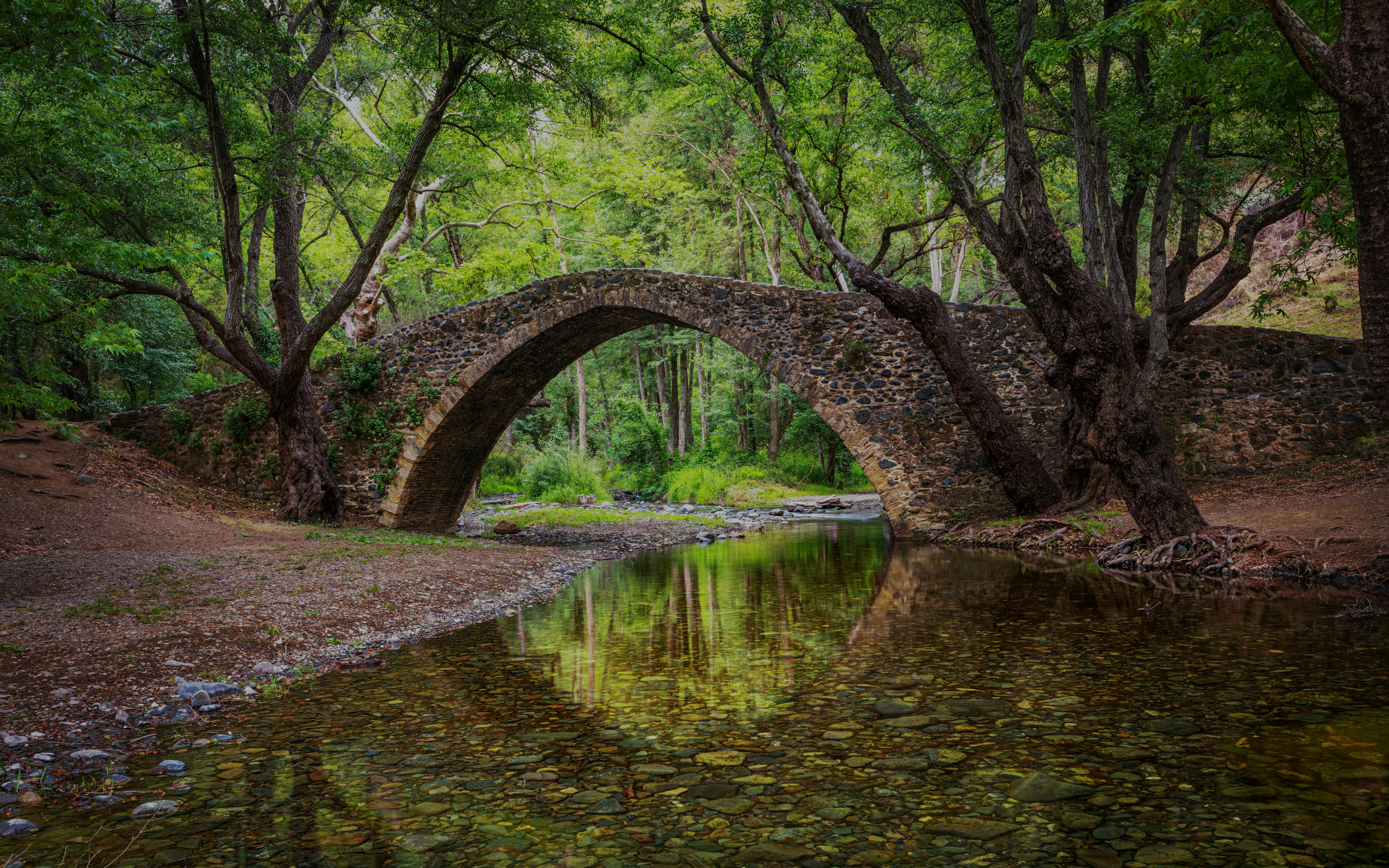 Kelefos Medieval Bridge in Cyprus reflected in a river, surrounded by lush trees.