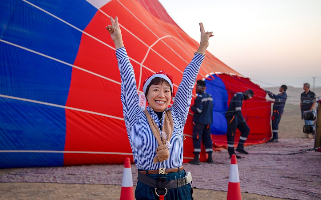 Person celebrating in front of a hot air balloon being prepared in Ras Al Khaimah.