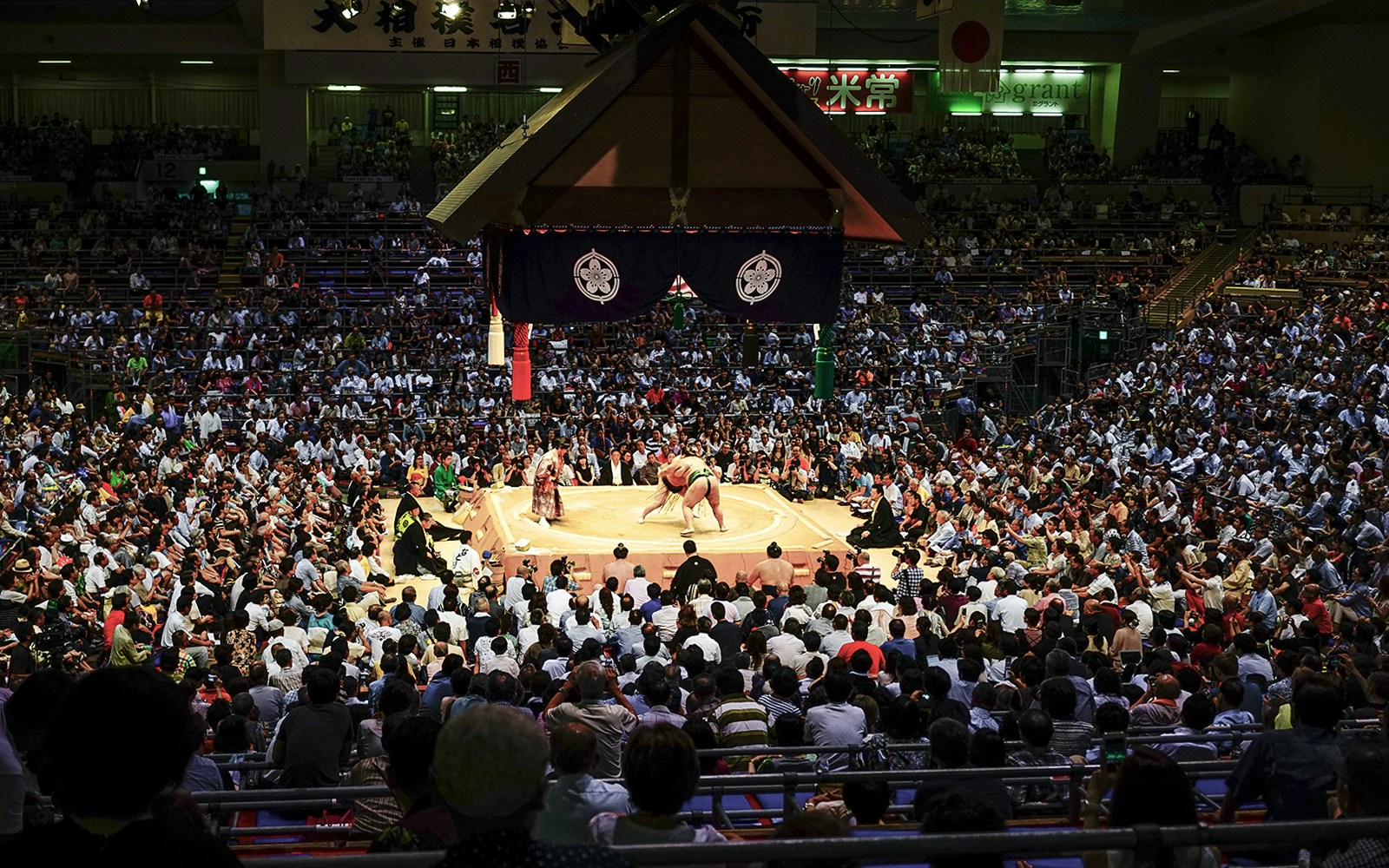 Sumo wrestlers competing in a packed arena during a tournament in Osaka.