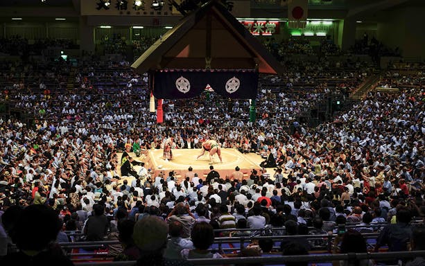 Sumo wrestlers competing in a packed arena during a tournament in Osaka.
