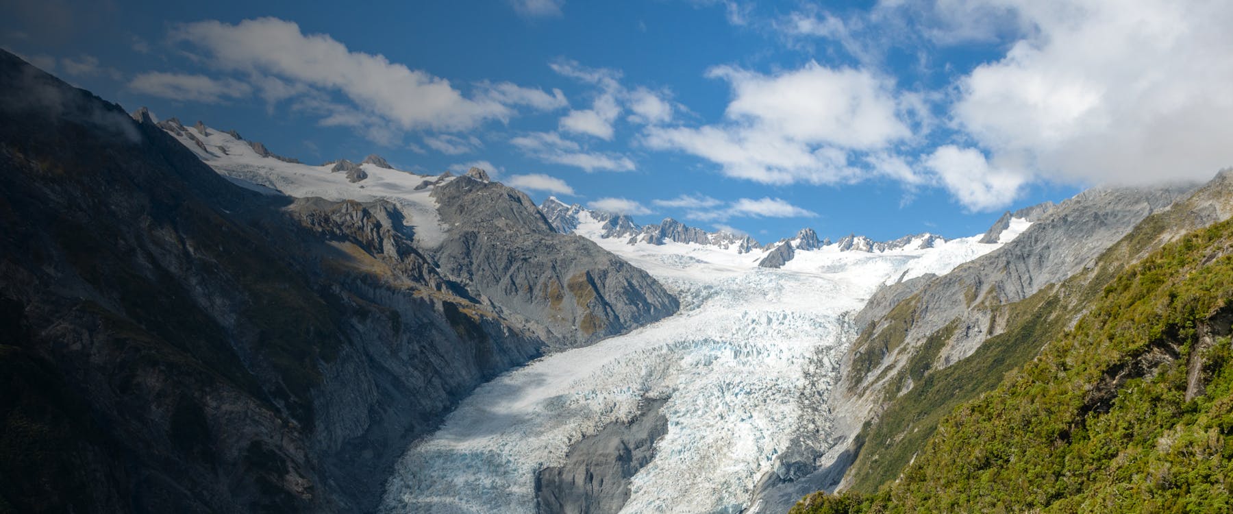 Fox Glacier in New Zealand with surrounding mountains and blue sky.