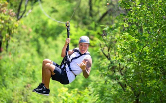 Person ziplining through lush forest with modern braking system.