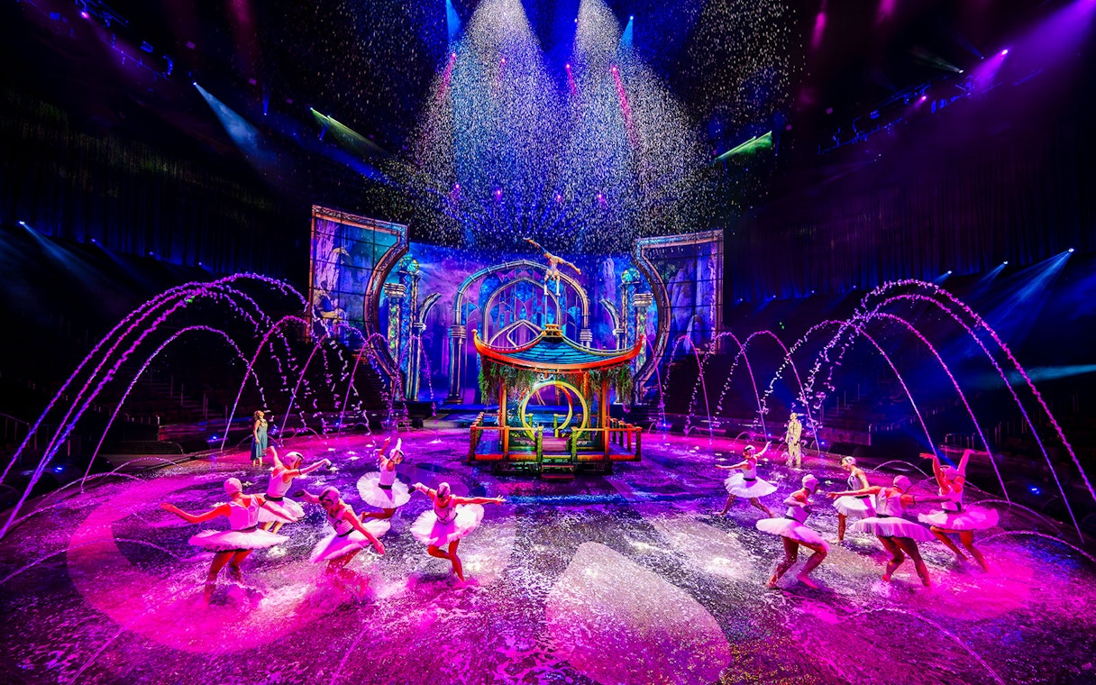 Performers in water dance at House of Dancing Water show, vibrant stage with fountains.