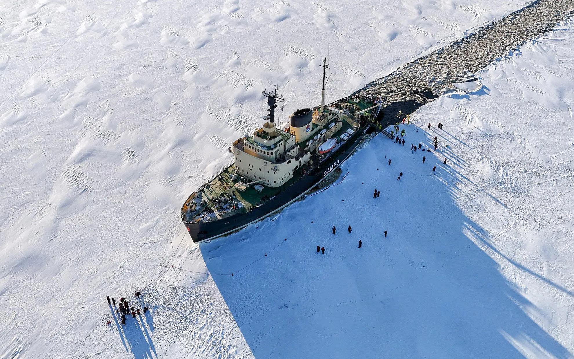 Icebreaker Sampo navigating frozen sea with tourists on ice during morning cruise.
