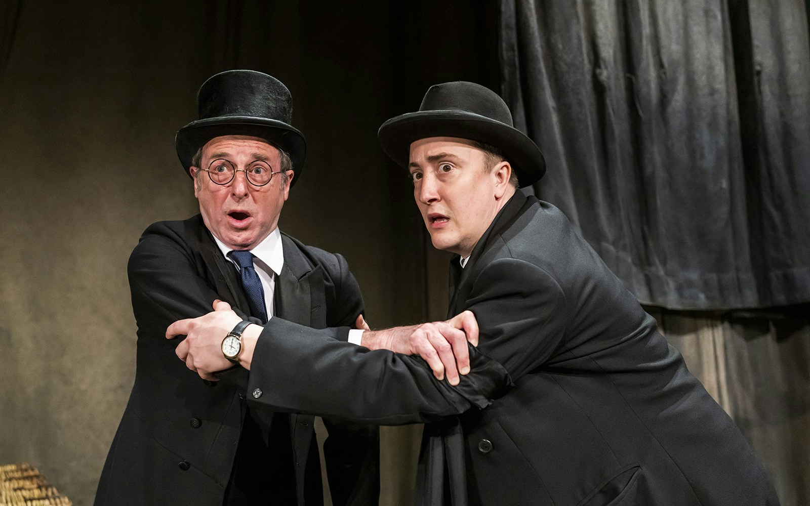 Two actors in Victorian attire express fear in a scene from "The Woman in Black" play.