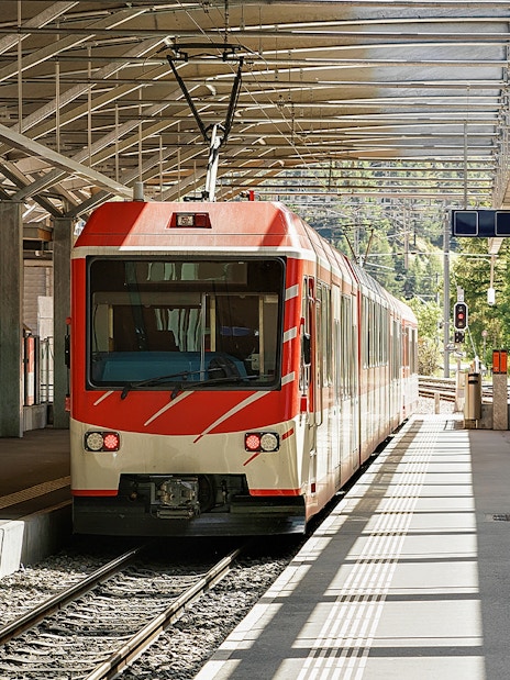 Zermatt shuttle train at station platform with scenic mountain backdrop.