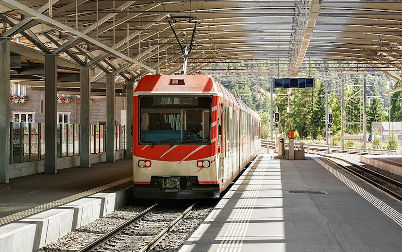 Zermatt shuttle train at station platform with scenic mountain backdrop.
