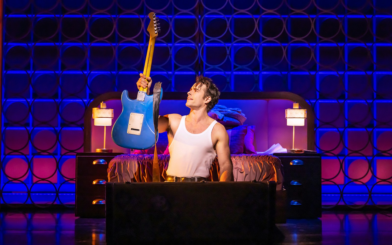 Performer holding a blue electric guitar on stage during "The Heart of Rock and Roll" show.