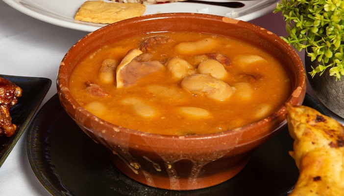Clay bowl of Judías del Barco stew with beans and meat.