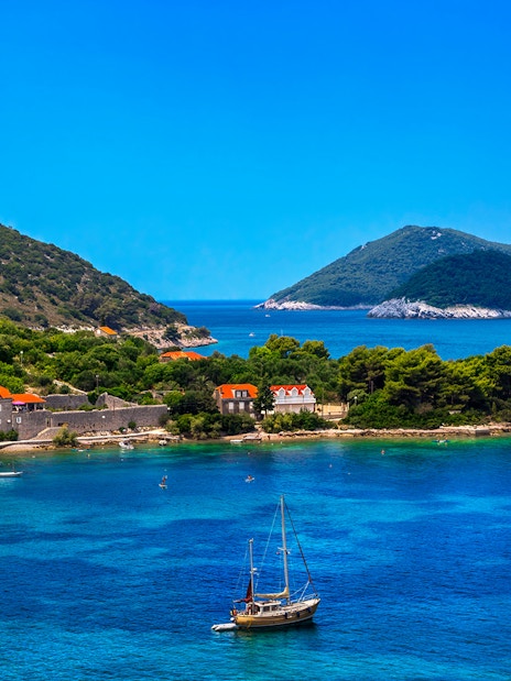 Sailboats near lush Elaphite Islands coast on Dubrovnik island-hopping cruise.