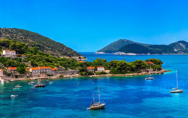 Sailboats near lush Elaphite Islands coast on Dubrovnik island-hopping cruise.