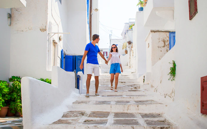 Couple walking through narrow whitewashed street in Mykonos, Greece.