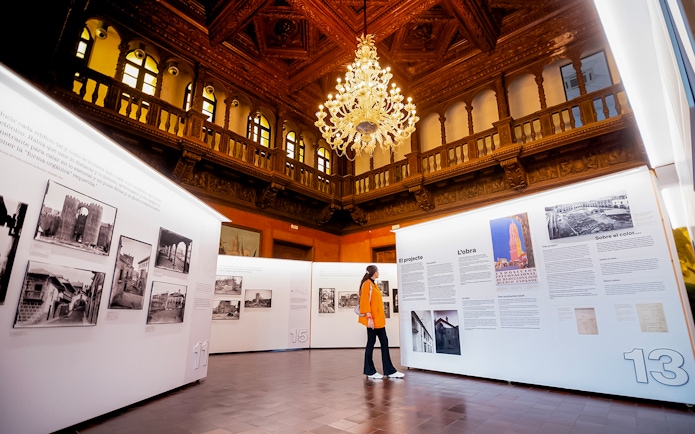 Visitor exploring an exhibition inside Poble Espanyol, Barcelona, with ornate ceiling and chandelier.