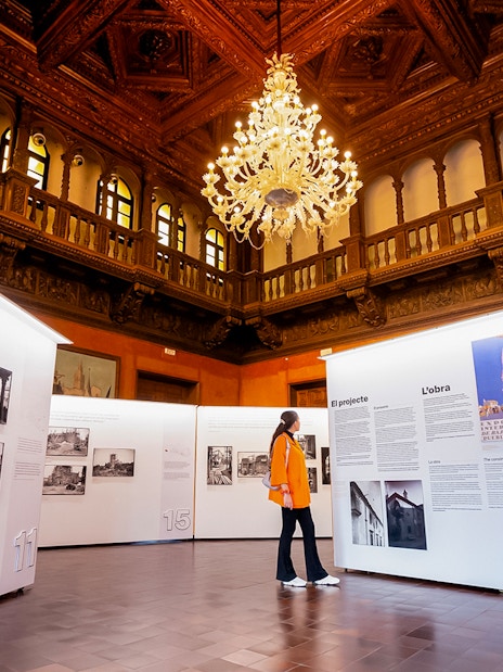 Visitor exploring an exhibition inside Poble Espanyol, Barcelona, with ornate ceiling and chandelier.