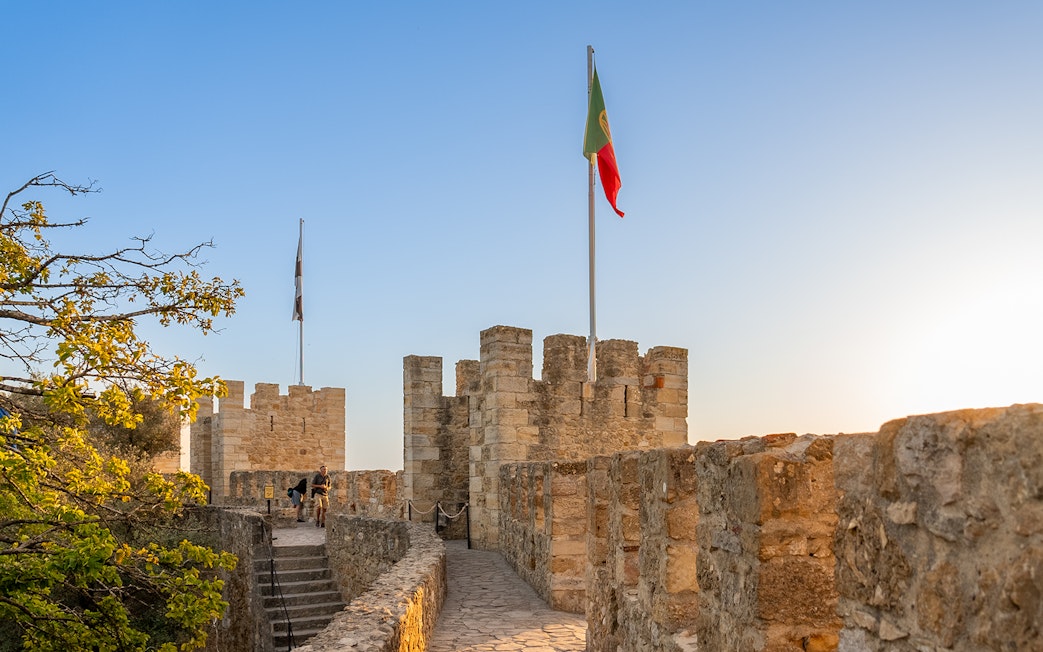 St. George’s Castle walls with Portuguese flag at sunset, Lisbon.