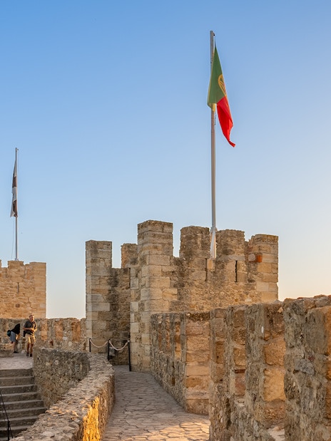 St. George’s Castle walls with Portuguese flag at sunset, Lisbon.