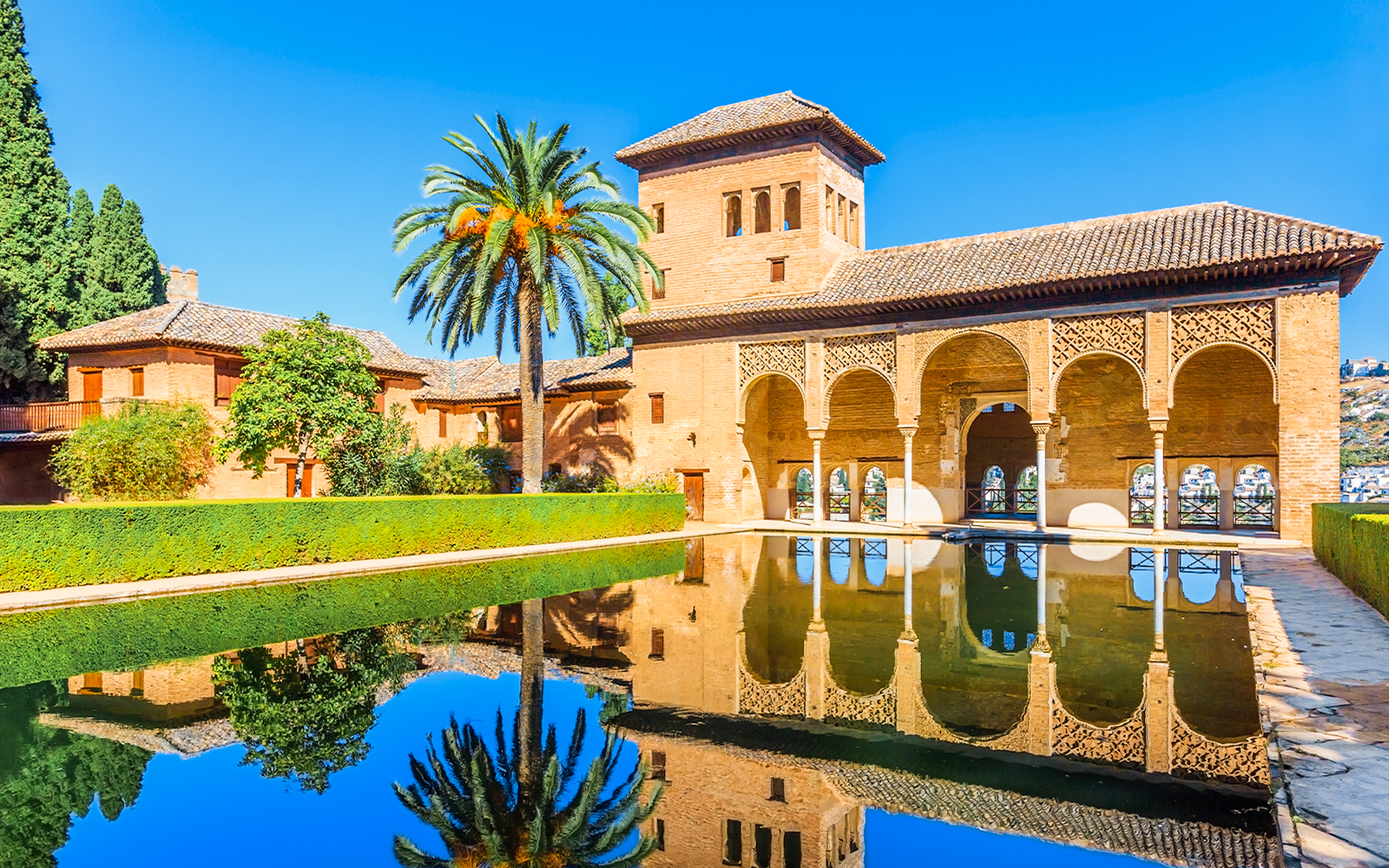 Alhambra palace reflecting in pool on a sunny day in Granada, Spain.