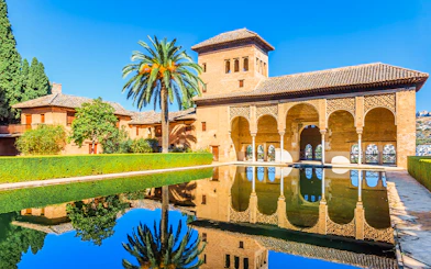 Alhambra palace reflecting in pool on a sunny day in Granada, Spain.